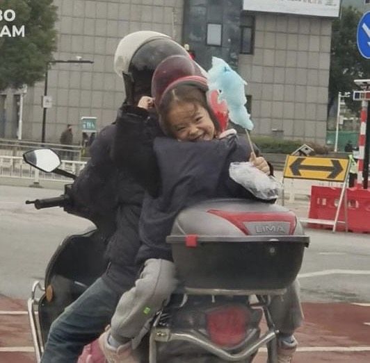 Ngồi sau xe, cô bé không quên chia sẻ kẹo bông gòn ngọt ngào cho cha