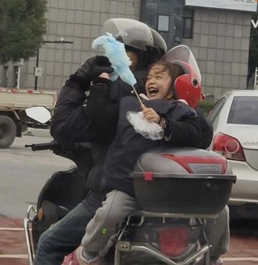 Trời mưa tầm tã, em bé luýnh quýnh nhướn người che chắn yên xe cho bố