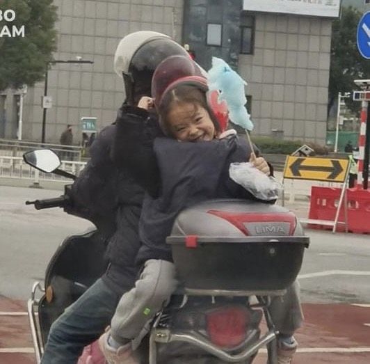 Trời mưa tầm tã, em bé luýnh quýnh nhướn người che chắn yên xe cho bố